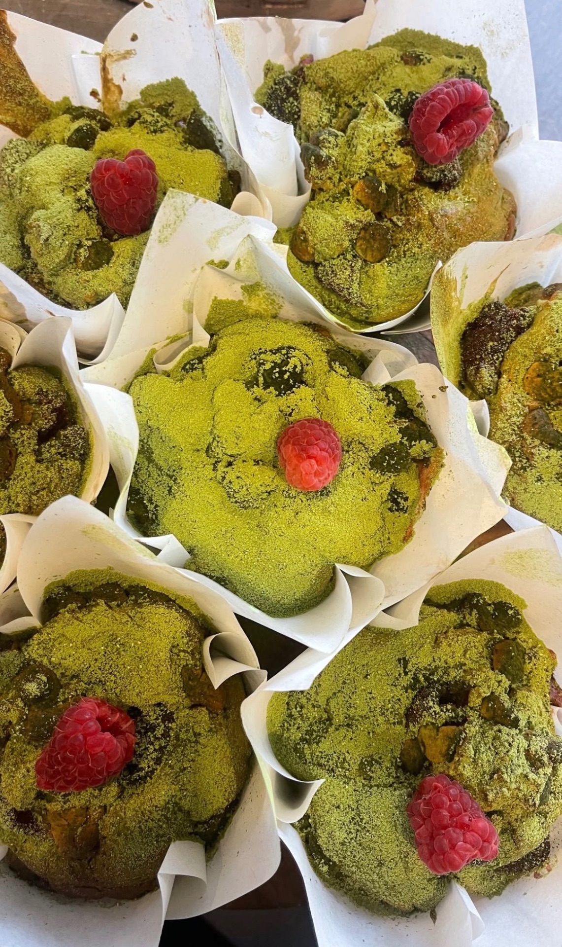 Tray of matcha pistachio muffins dusted with matcha and topped with raspberries