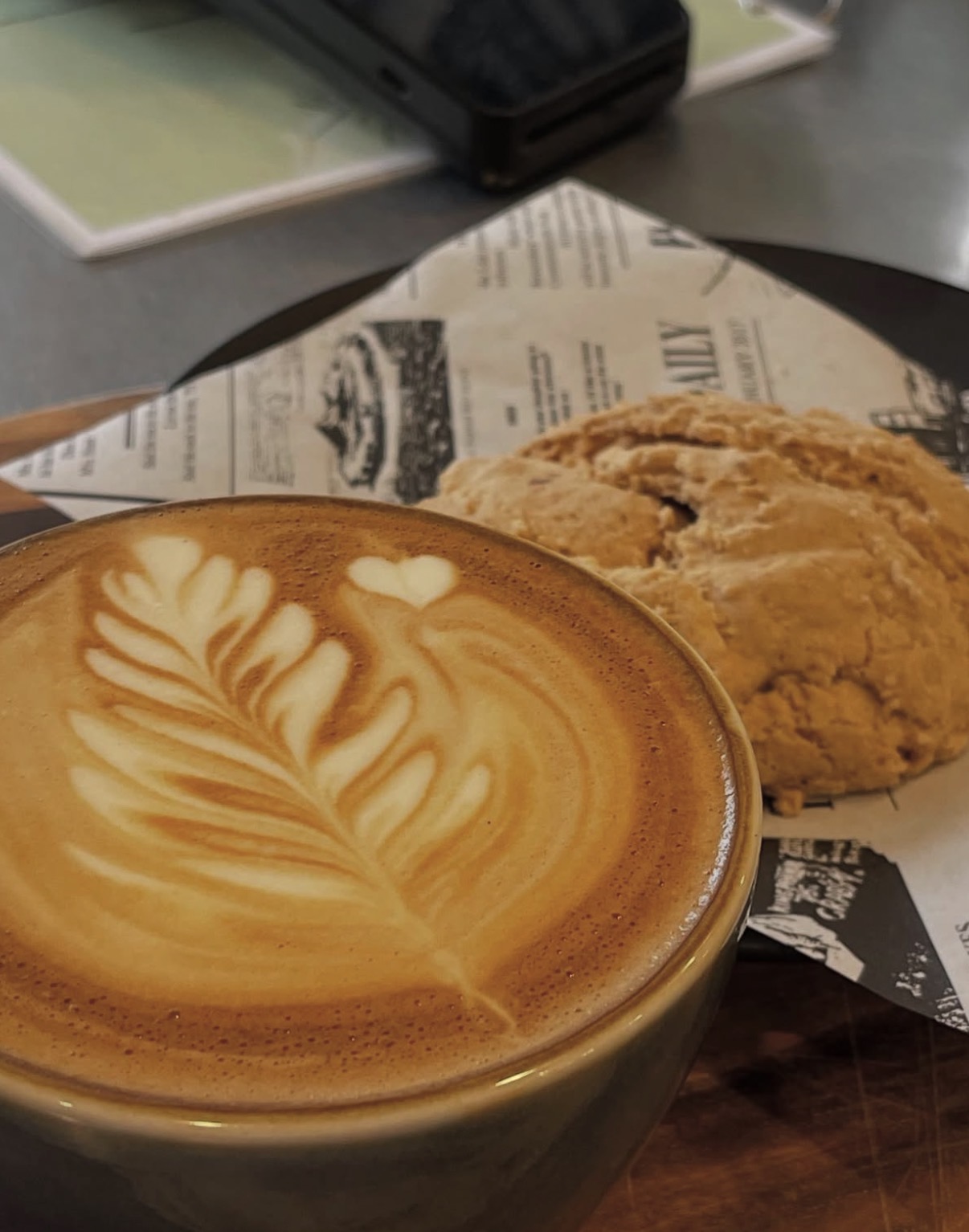 Flat white with rosetta latte art beside a house-baked cookie on newsprint
