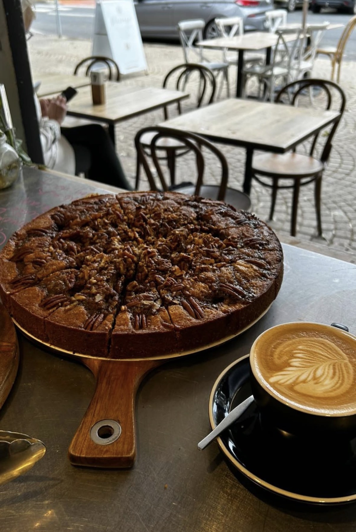 Whole pecan cake on a timber board beside a latte with rosetta art