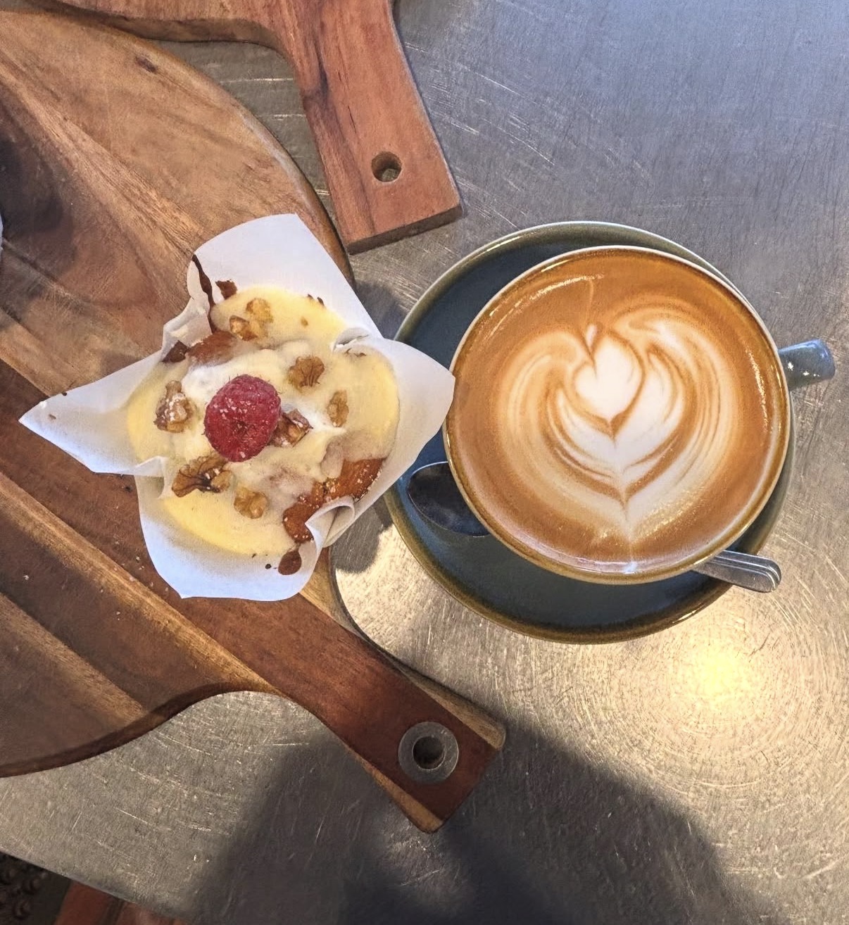 Raspberry walnut muffin on a timber board next to a flat white with heart latte art