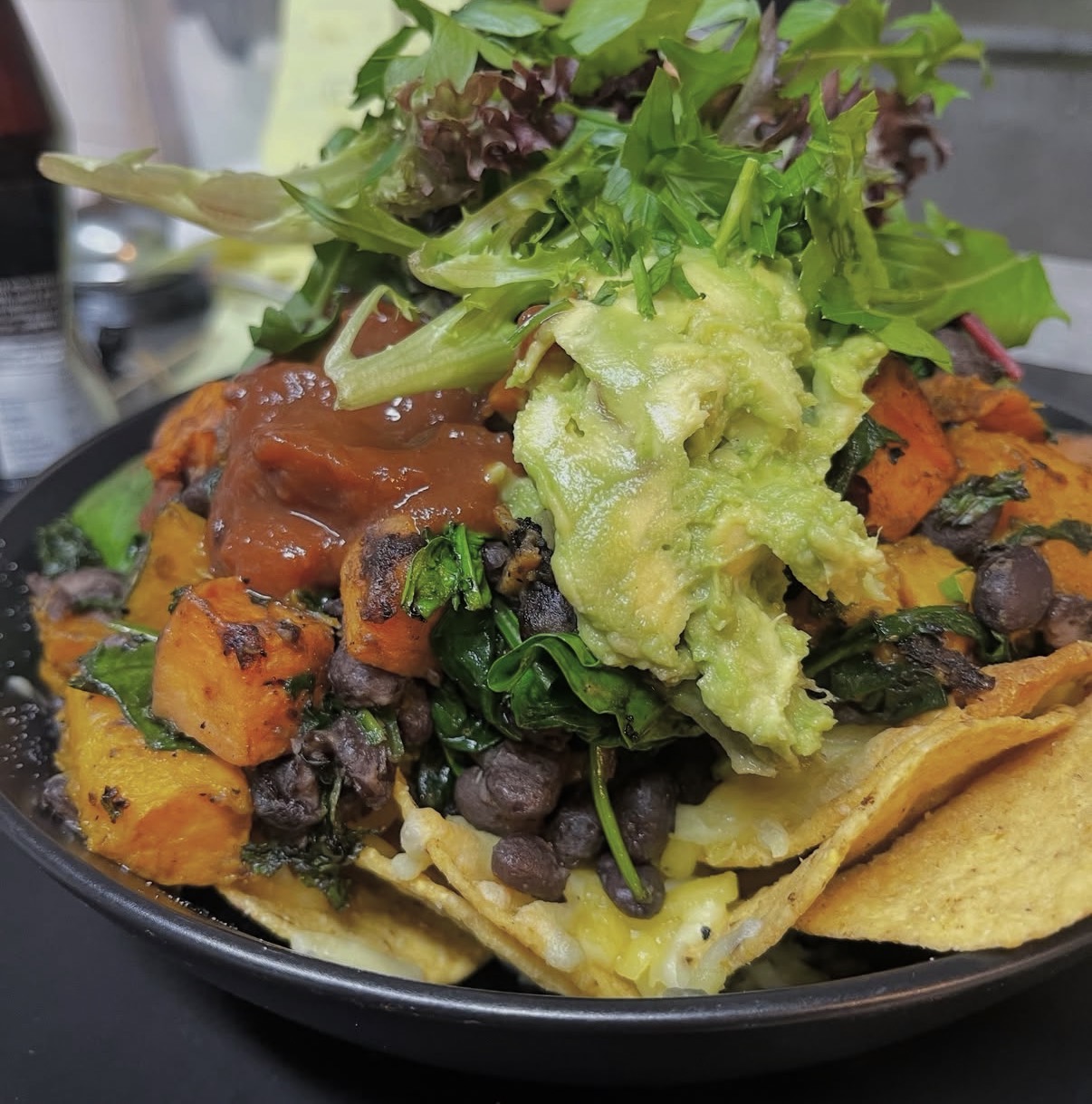 Loaded nachos with roast pumpkin, black beans, guacamole and salsa topped with leaves