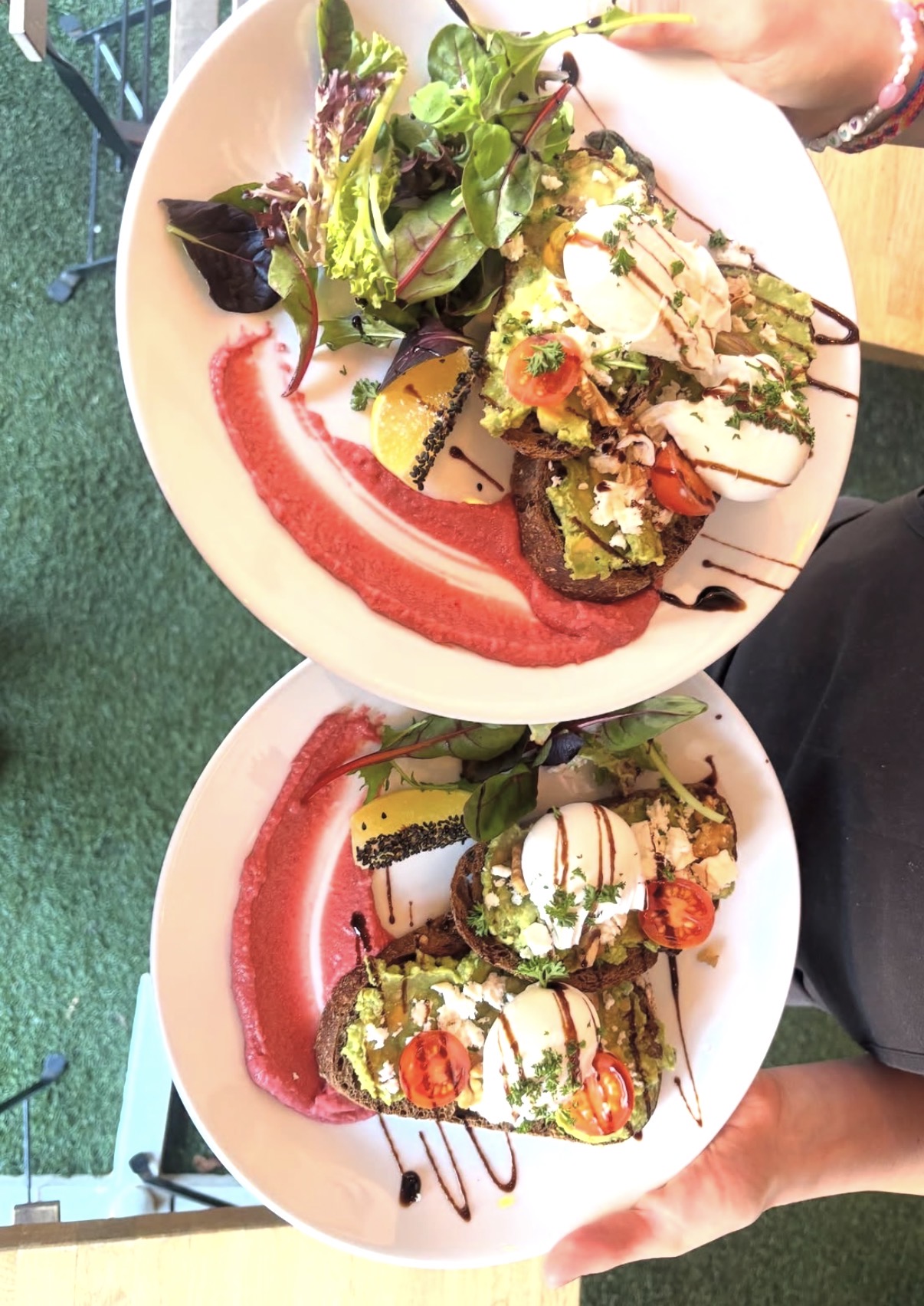 Two plates of smashed avocado toast with poached eggs, feta and beetroot puree